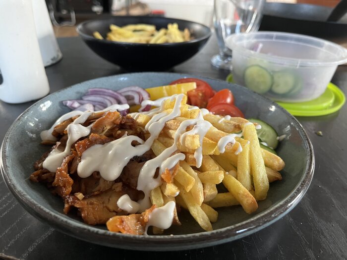 Kebabtallrik med kyckling, pommes frites, grönsaker och vit sås på en tallrik.