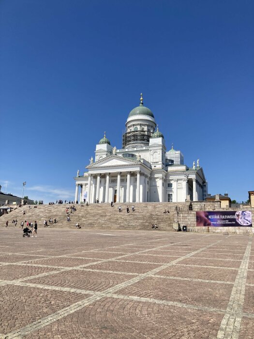 Domkyrka med kupol och trappor framför, människor och en klarblå himmel.