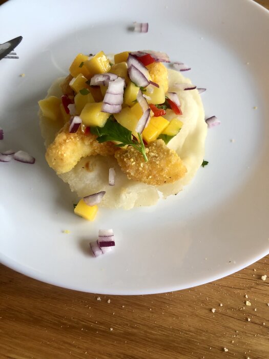 Fisktacos med mango, rödlök och sås på ett tjockare bröd på vit tallrik.