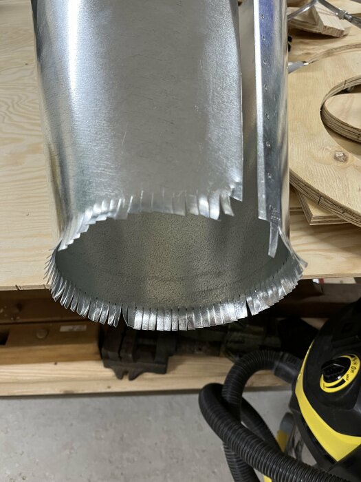 Metallkon med klippta flärpar i botten och nitar längs en sida på arbetsbänk.