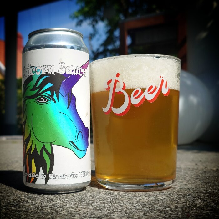 Burk med Unicorn Sauce NEIPA från Hop Notch Brewing bredvid ett ölglas med skum på en utomhusyta.