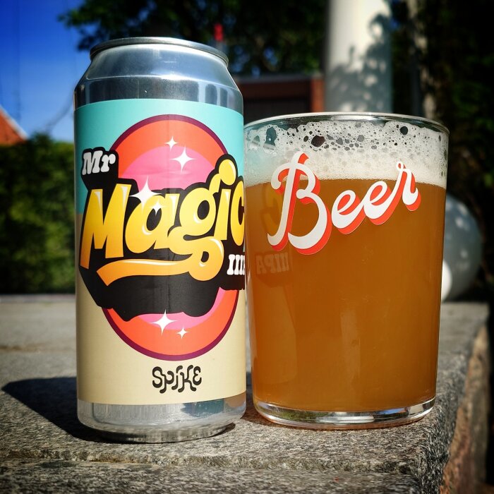 En burk Triple IPA-öl märkt "Mr. Magic" och ett glas med skummande öl bredvid, utomhus i solsken.