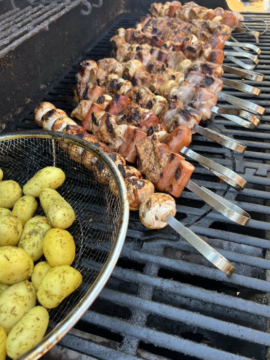 Grillad mat på en grill med spett med kött och korv samt en korg med kryddade stekta potatisar.