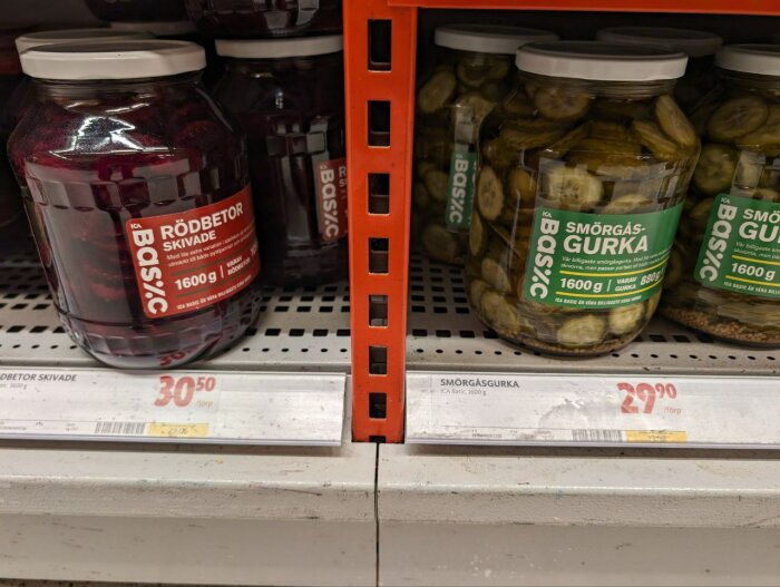 Burkar med syltade rödbetor och smörgåsgurka på en butikshylla, prislappar synliga.