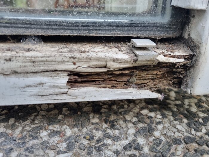 Nedre delen av en altandörr med murket trä och en skadad metallist tydligt synligt mot en stenbelagd grund.