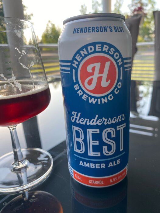 En burk Henderson's Best Amber Ale bredvid ett glas fylld med rödbrun öl på ett bord.