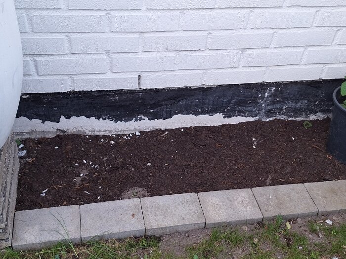 Husgrund med vit färg som flagar av och avtäckt svart område nära marken.