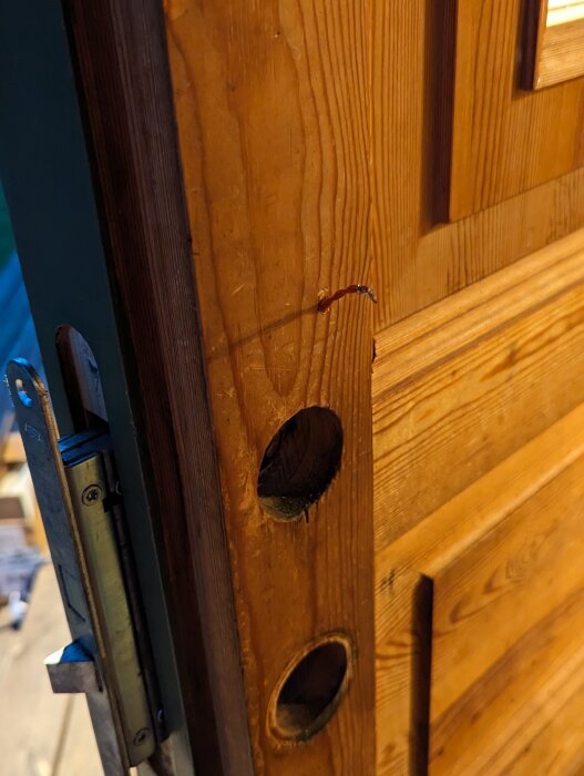 En delvis demonterad ytterdörs låsmechanism med synliga kablar och hål för installation av en smart dörrkontakt.