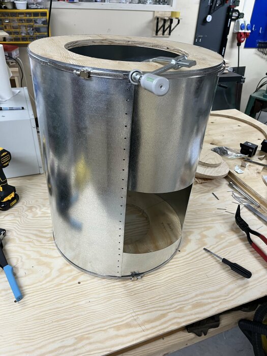 En metallcylinder med en öppen nedre del och verktyg på ett träbord.