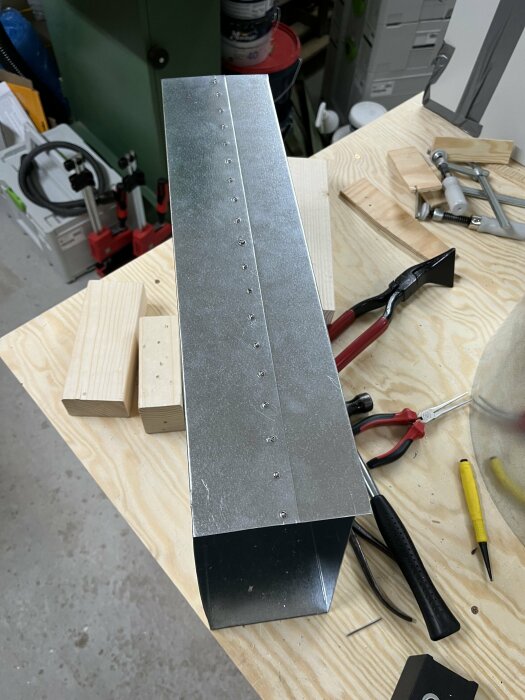 Metallplåt med borrhål och nitar på ett arbetsbord med verktyg.