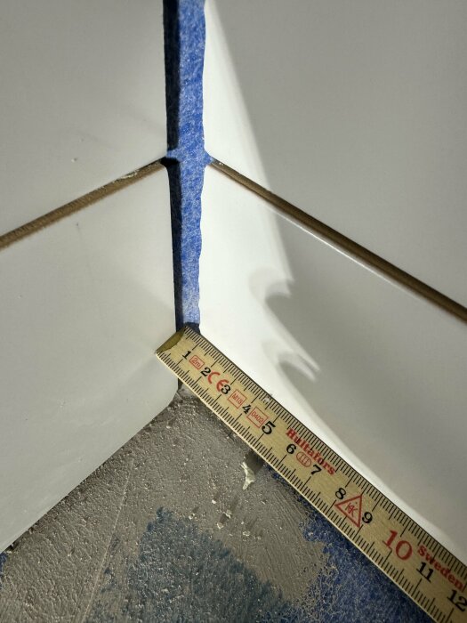 Kakelsättning i badrum med tätskiktsfolie som spänner ut från hörnet, mätsticka syns vid foten.