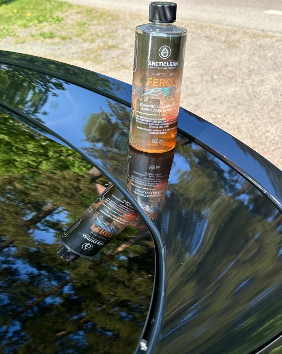 Flaska med bilvårdsschampo Ferox står på blank bilhuv som reflekterar träd och himmel.