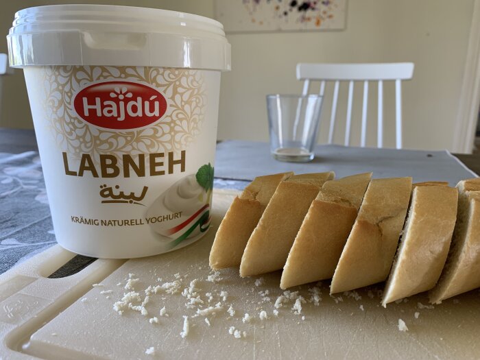 En burk Hajdú Labneh krämig naturell yoghurt och skivat vitt bröd på ett skärbräde.