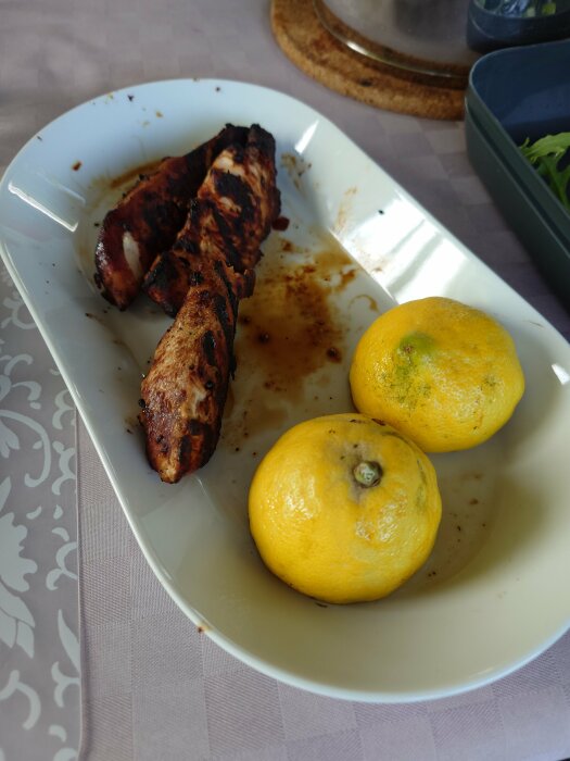 Grillad kycklingfilé med kryddor och två grillade citronhalvor på en vit tallrik.