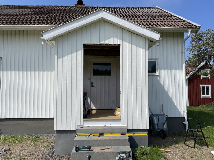 Nyuppsatt vit panel på verandan av ett hus med verktyg framför.