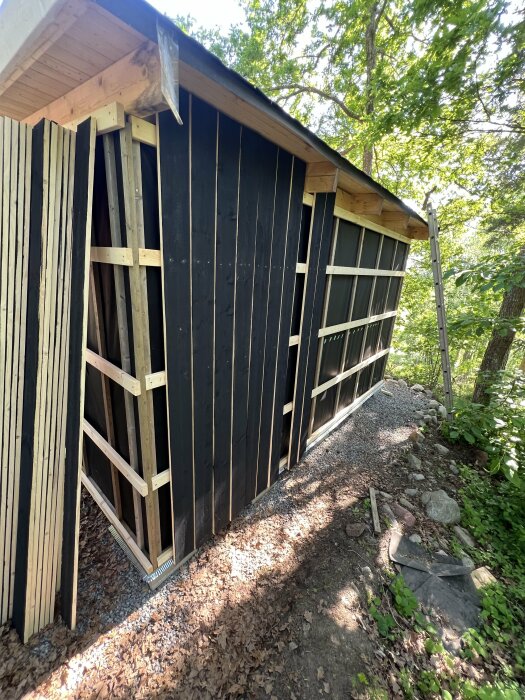 Fristående byggnad under konstruktion med nyuppsatt svart panel och synliga träreglar på en solig dag.