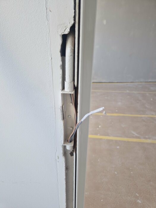 Öppning i vägg där därrfoder tagits bort visar exponerade kablar och fäste för strömbrytare vid en lättbetongvägg.