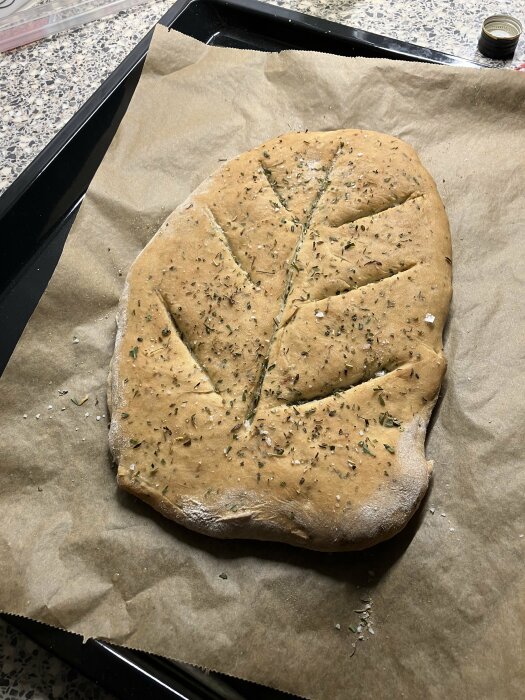 Nybakat örtbröd med franska örter och vitlök, insnitt för portioner, på bakplåtspapper.