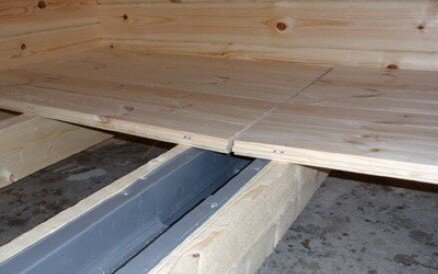 Värmebehandlade träplankor monterade över en vattenränna i en pågående bastubyggnation.