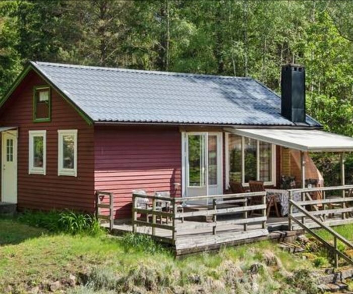 Ett rött enplanshus med veranda och plåttak i skogsmiljö, frågeställning om påbyggnad.