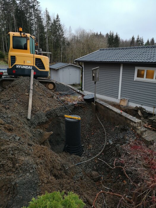 Grävmaskin vid tomtgränsen för grävningsarbete nära en husgrund och ny brunnsinstallation.