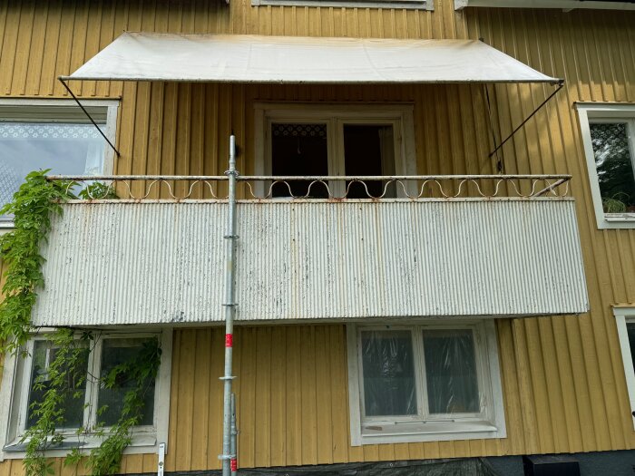 Gammal balkong med synligt rostigt armeringsjärn och skadad sinusplåt på ett hus byggt 1950.