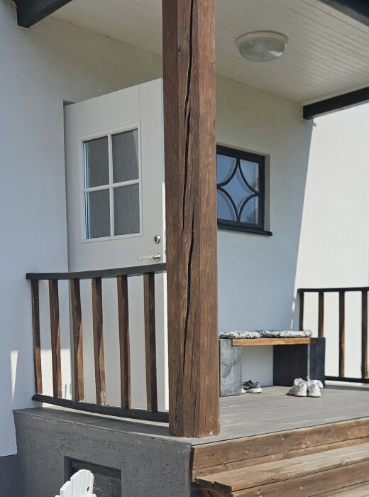 Sprucken träpelare på balkong med träräcke och ytterdörr i bakgrunden.