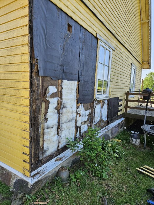Gammalt hus med skadad fasad och exponerad glasullsisolering där panelen tagits bort.