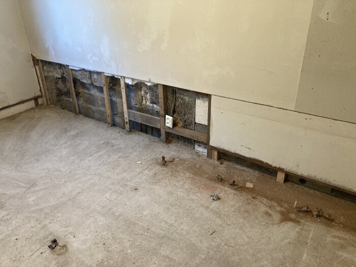 Renoveringsarbete i ett rum med delvis borttagen isolering och skadad vägg vid golvet.