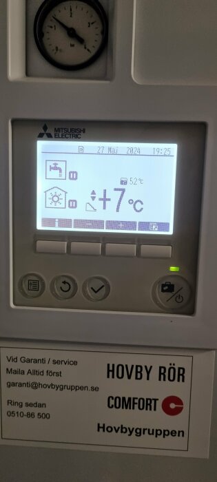 Digital termostat visar +7°C i ett hus, datum och tid, med kontaktinformation för Hövby Rör Comfort under displayen.