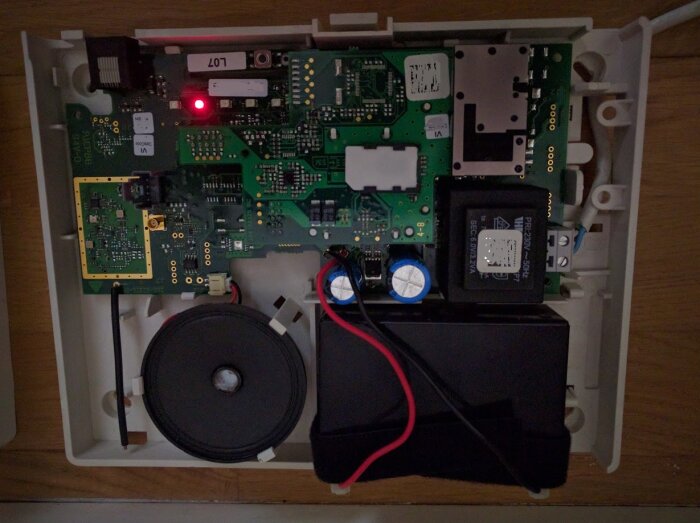Inre komponenter i ett larmsystem med kretskort, batteri och en tom SIM-kortshållare.