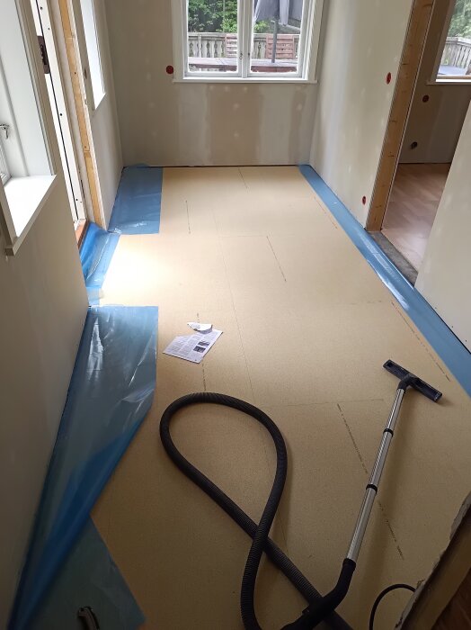Nyinstallerad brun golvunderläggning i ett rum med dammsugare och förpackningsmaterial på golvet.