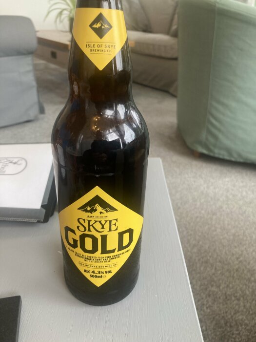 Flaska Skye Gold öl från Isle of Skye Brewing Co. står på ett bord framför en soffa.