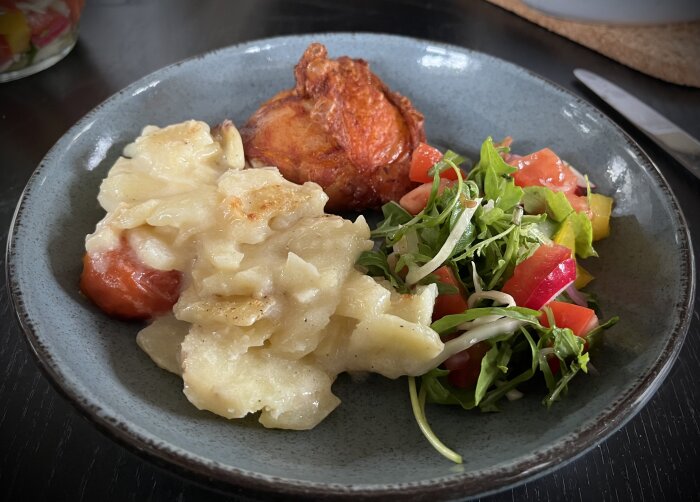 KycklinglÄrfilé med grÀddig potatisgratÀng och fÀrsk grönsallad pÄ en grÄ tallrik.