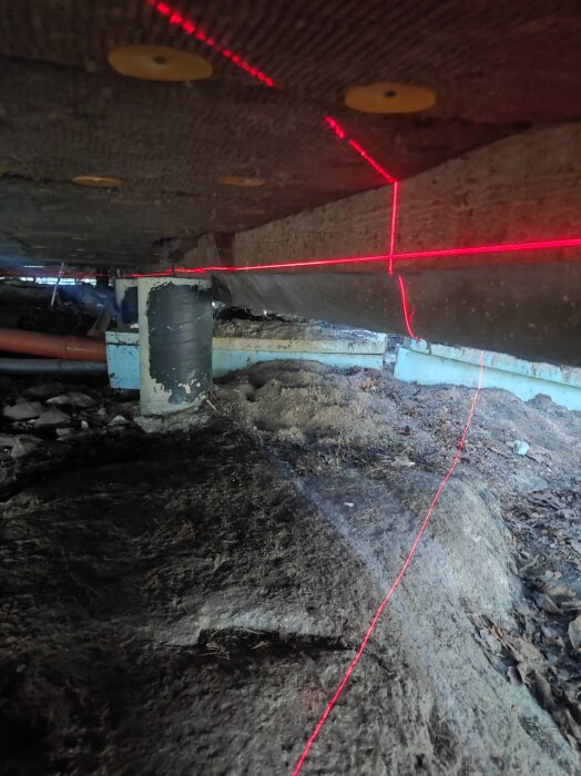 Undersida av golv med träbalkar som bågnar, synlig plint och laserlinje som visar ojämnheter.