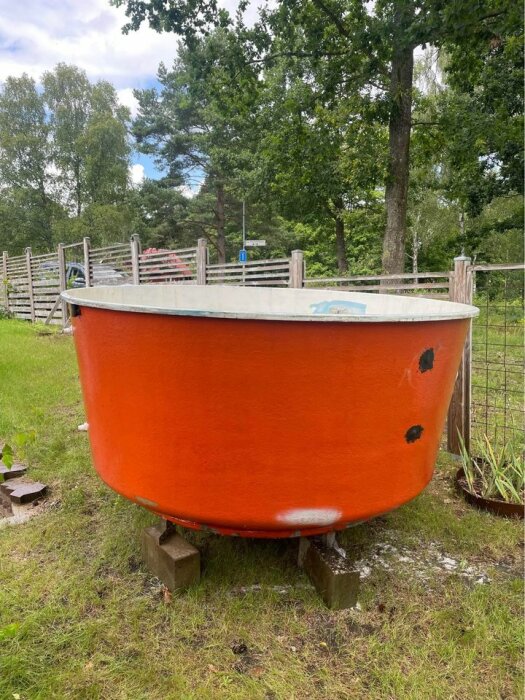 Orange glasfiberbalja på betongblock i en trädgård, cirka 3 meter i diameter.