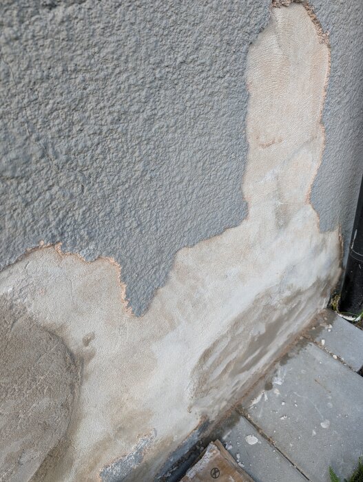 En vägg med skadad yttre puts som visar underliggande slätare lager.