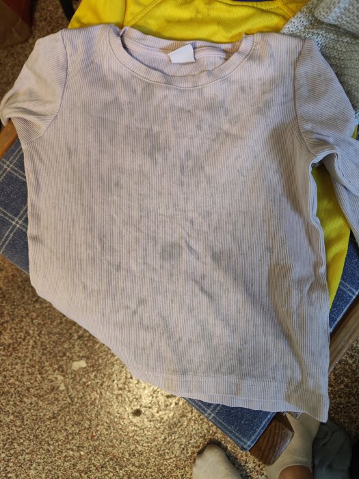 Vitt plagg med grå fläckar ligger ovanpå andra tvättade kläder, indikerar problem med tvättmaskin.