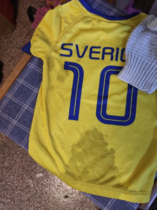 Fläckar på en gul Sverige-fotbollströja efter tvätt. Ströjan ligger på en blå och vit rutig yta.