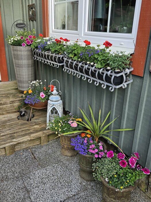 Blomsterarrangemang vid entré med krukor och en väggmonterad blomlåda under fönster.