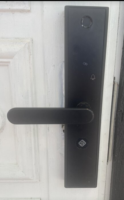 Dörrhandtag med elektroniskt kodlås och dold nyckelhål under löstagbar bricka på vit dörr.
