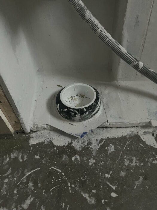 Nytt wc-avlopp med inkorrekt höjd och problematisk koppling, synligt i en nyligen bilad toaletthörna med damm och rörmokaravfall.