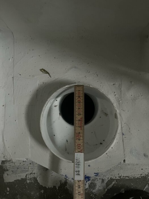 Vy över ett nyinstallerat wc-avlopp i betonggolv med ett måttstock som visar avståndet till det färdiga golvet.