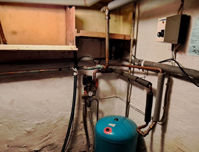 Källare med äldre värme- och avloppsrör, viss oxidationsfläck visas, vid en varmvattenberedare.