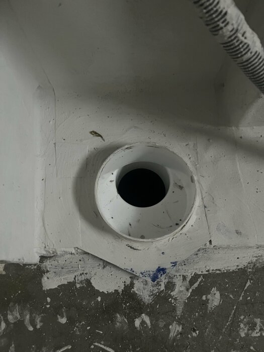 Nyinstallerat vit WC-avloppsrör nära vägg, med synlig förminskning och befintligt grått rör.