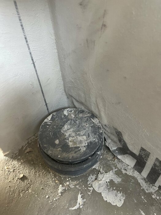 En felplacerad och för lågt installerad avloppskoppling nära en vägg i betong, omgiven av spackel och byggsmuts.