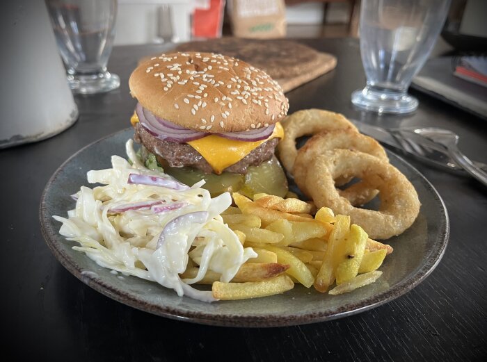 Hamburgare med ost och lök, pommes frites, lökringar och coleslaw pÄ en tallrik.