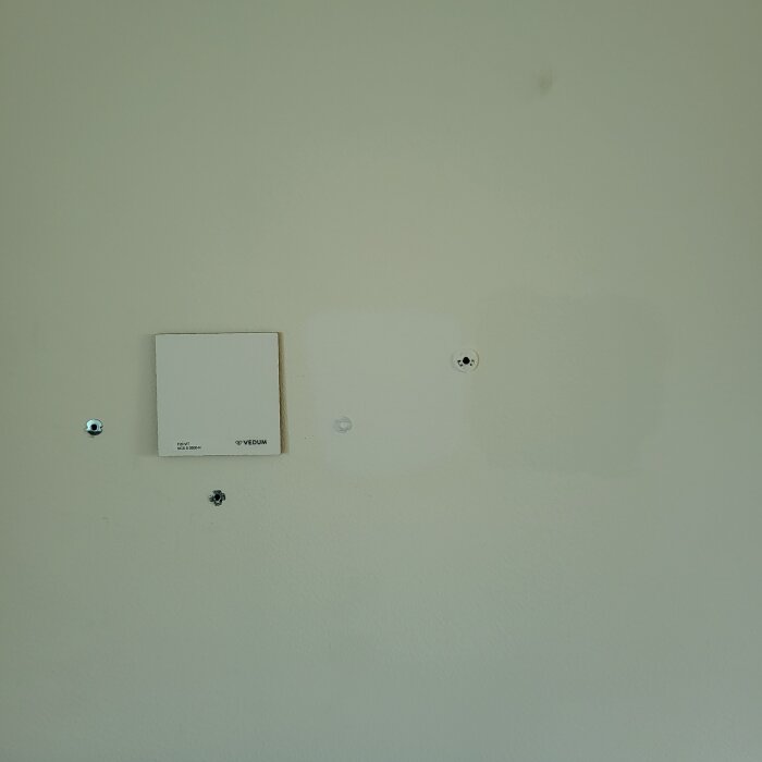 Vägg med provmålade kvadrater i olika vita nyanser för jämförelse mot befintlig väggfärg.