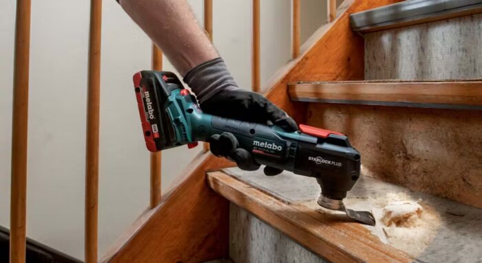 Hand med multiverktyg tar bort skadad del av trästeg på trappa.