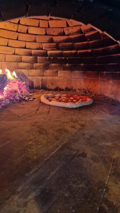 Pizza gräddas i en hembyggd tegelugn med en eld brinnande intill.